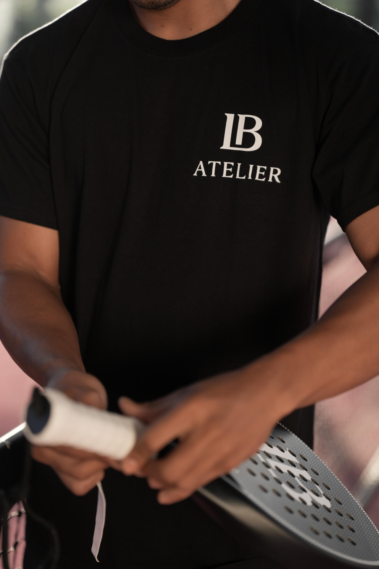 A player in an LB Atelier shirt wrapping a fresh grip on a racket
